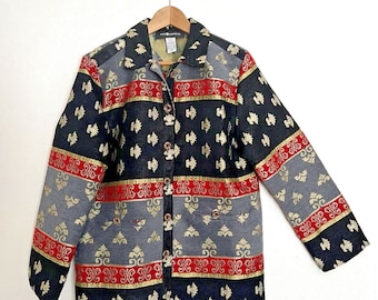 May include: A button-down jacket with a striking pattern. The jacket features a black background with gold, red, and gray accents. The design includes repeating gold floral motifs and decorative bands. The jacket is hanging on a wooden hanger.