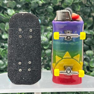 May include: Two miniature skateboards. One is black with grip tape and the other is a rainbow design with a yellow sun graphic. Both have silver trucks and yellow wheels.