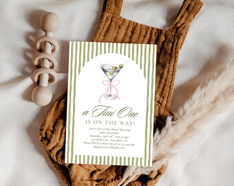 May include: A baby shower invitation with a martini glass illustration, olive green stripes, and the text "a Tini One IS ON THE WAY!". The invitation is on a brown onesie with a wooden rattle and dried grass.
