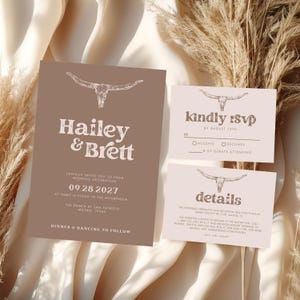 May include: A set of wedding stationery in a rustic theme. The invitation features the names "Hailey & Brett" and event details. The RSVP and details cards are included, all with a steer skull illustration and a neutral color palette.