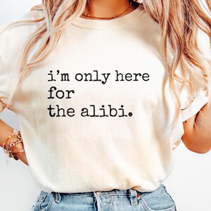 May include: A white t-shirt with the text "i'm only here for the alibi." printed in black.