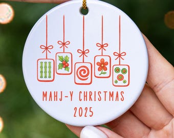 May include: Round white ceramic Christmas ornament with red illustrations and text. The ornament has hanging rectangular designs with patterns and the words "MAHJ-Y CHRISTMAS 2025" in red.