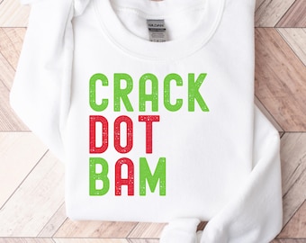 May include: White sweatshirt with the words "CRACK DOT BAM" in green and red block letters. The sweatshirt is made of a soft material and has a crew neck. The background is a light brown wood.