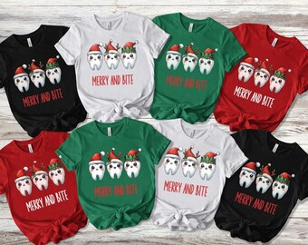 May include: Eight t-shirts with a Christmas-themed design featuring three cartoon teeth wearing Santa hats and elf hats. The text "Merry and Bite" is printed on each shirt.