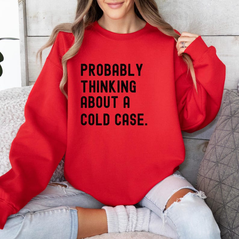May include: Red sweatshirt with the text "PROBABLY THINKING ABOUT A COLD CASE." printed in black.