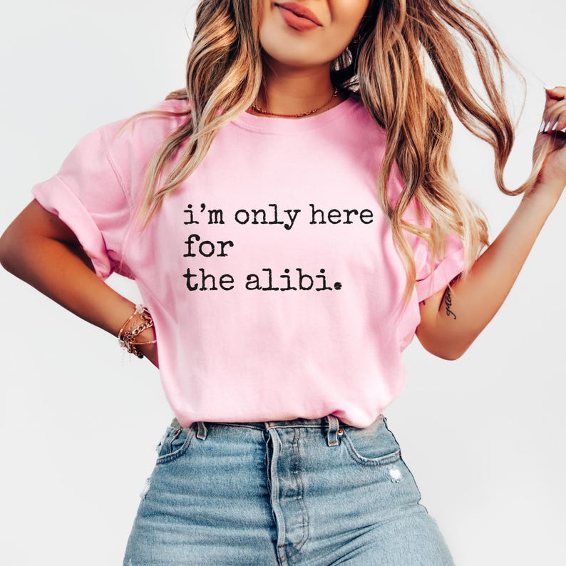 May include: Pink t-shirt with the text "i'm only here for the alibi." printed in black.