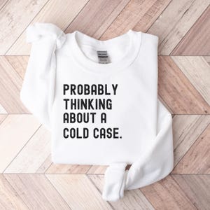 May include: White sweatshirt with black text that reads "PROBABLY THINKING ABOUT A COLD CASE."