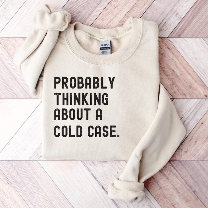 May include: A beige sweatshirt with the text "PROBABLY THINKING ABOUT A COLD CASE." printed in black.