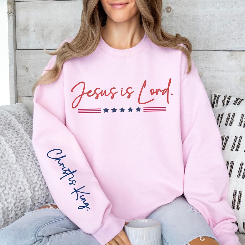 May include: Pink sweatshirt with the text "Jesus is Lord." in red and "Christ is King." in blue on the sleeve. The sweatshirt has a red, white, and blue stripe with five stars.