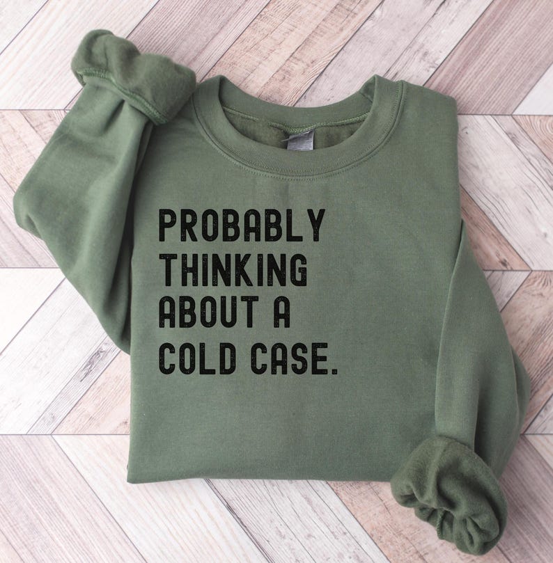 May include: A green sweatshirt with the text "PROBABLY THINKING ABOUT A COLD CASE." printed in black.