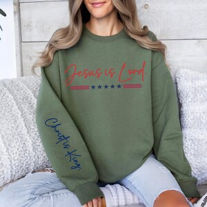 May include: A green sweatshirt with the text "Jesus is Lord" in red and white with stars and stripes. The left sleeve has the text "Christ is King" in blue.