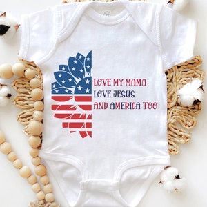 May include: White baby onesie with a red, white, and blue sunflower design. The text "LOVE MY MAMA LOVE JESUS AND AMERICA TOO" is printed on the onesie.