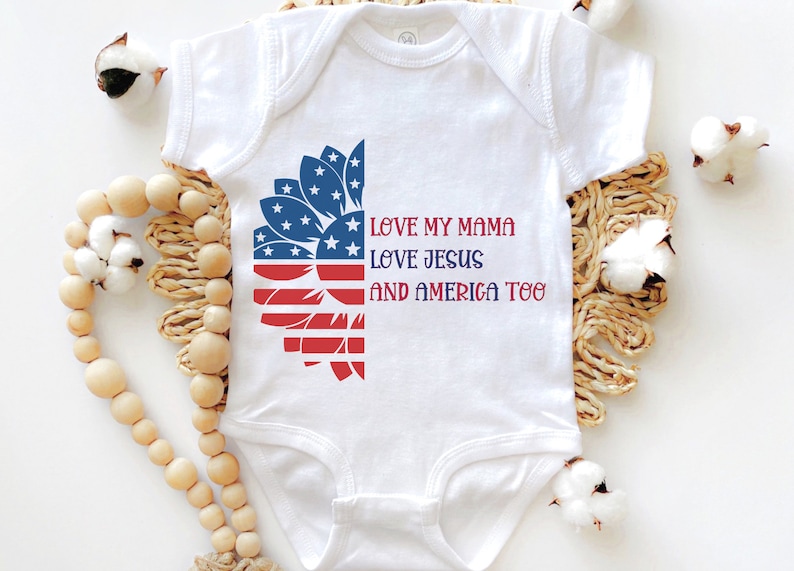 May include: White baby onesie with a red, white, and blue sunflower design. The text "LOVE MY MAMA LOVE JESUS AND AMERICA TOO" is printed on the onesie.