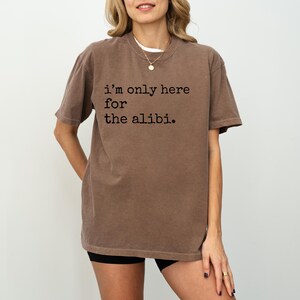 May include: A brown t-shirt with the text "i'm only here for the alibi." printed in black.