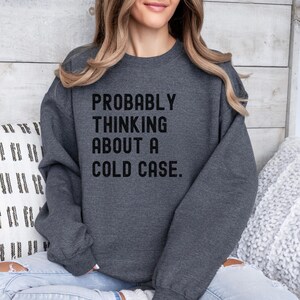 May include: A dark gray sweatshirt with the text "PROBABLY THINKING ABOUT A COLD CASE." printed in black.