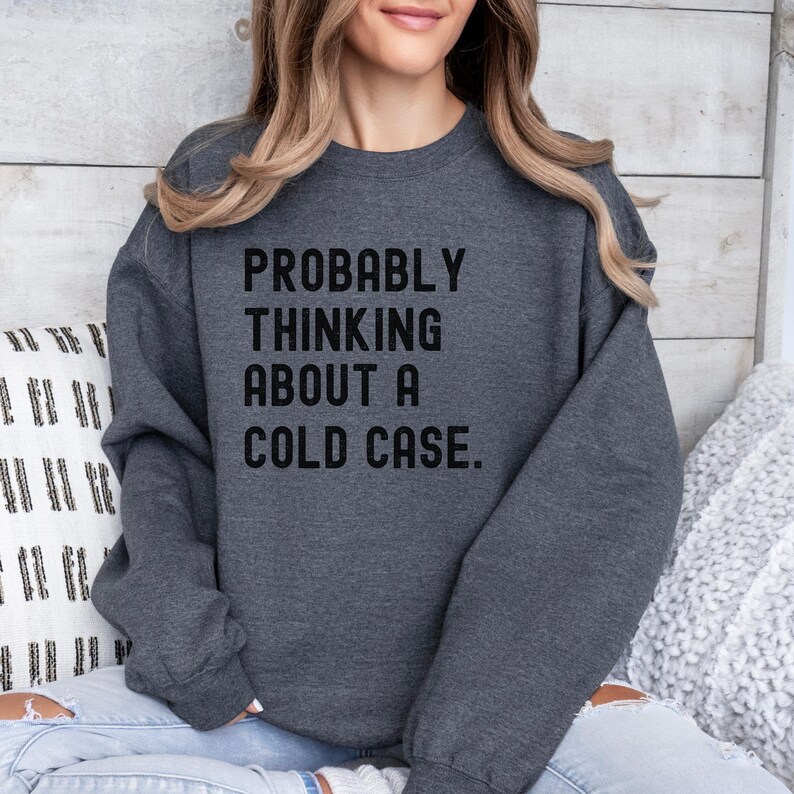 May include: A dark gray sweatshirt with the text "PROBABLY THINKING ABOUT A COLD CASE." printed in black.