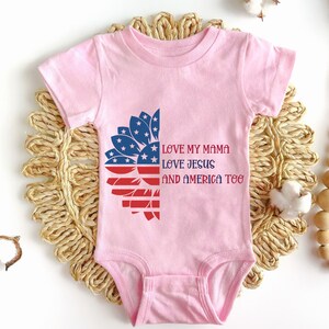 May include: Pink baby onesie with a red, white, and blue sunflower design. The text "Love my mama, Love Jesus, and America too" is printed on the onesie.