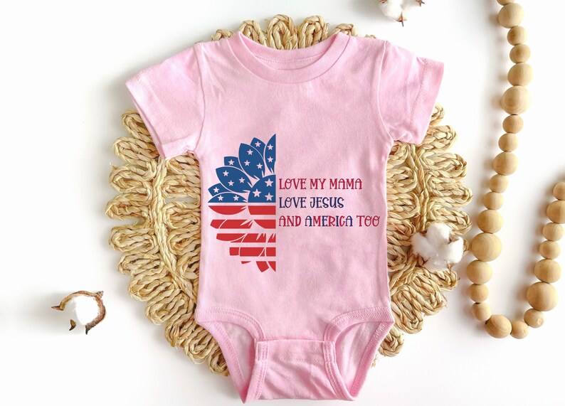 May include: Pink baby onesie with a red, white, and blue sunflower design. The text "Love my mama, Love Jesus, and America too" is printed on the onesie.