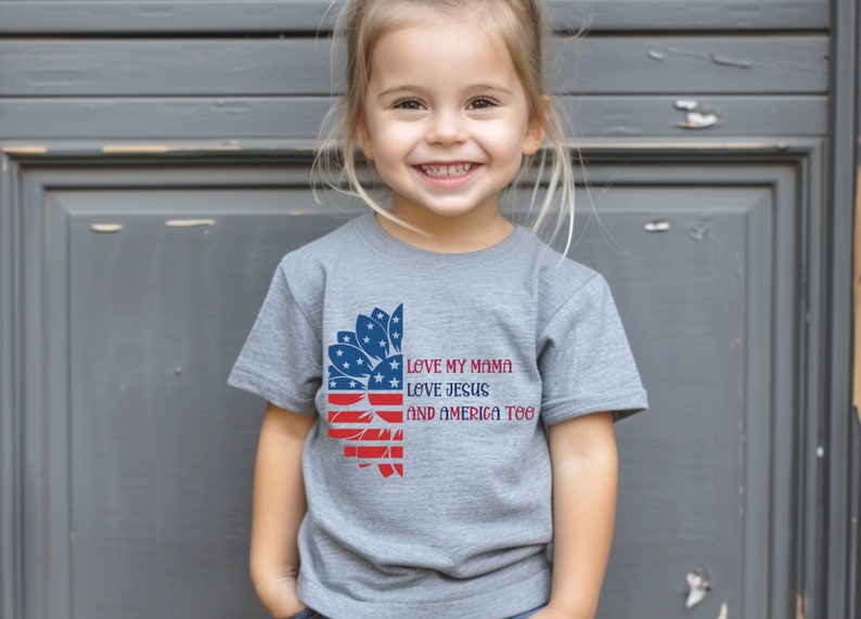 May include: A grey t-shirt with a red, white, and blue sunflower design. The text "Love my mama, Love Jesus, and America too" is printed on the shirt.