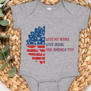 May include: A grey baby onesie with a red, white, and blue sunflower design. The onesie has the text "Love my mama, Love Jesus, and America too".
