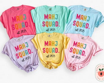 May include: Six colorful t-shirts with the text "MAHJ SQUAD. est 2025" in rainbow letters. The shirts are in various colors, including pink, light blue, yellow, and lavender.
