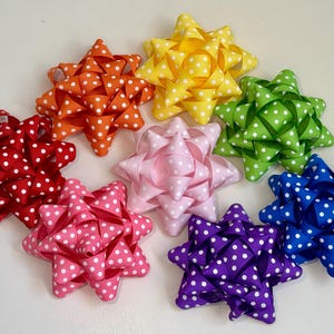 May include: Assortment of eight polka dot bows in various colors, including red, pink, yellow, green, blue, and purple. Each bow is made of ribbon with white polka dots.