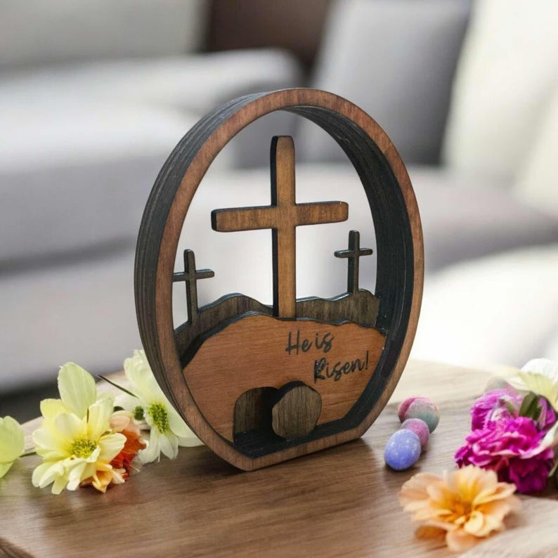 May include: Wooden Easter cross and tomb decoration with the text "He is Risen!"  The decoration is brown and features a cross with a tomb at the base.