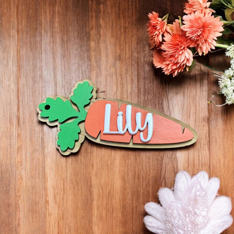 Peut inclure: Une pancarte en bois en forme de carotte avec un dessus vert feuillu et le nom "Lily" &eacute;crit en lettres blanches.