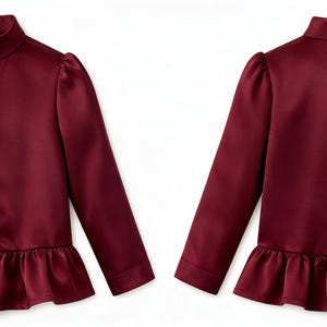 May include: A burgundy-colored blouse with a high collar and long sleeves. The blouse features a row of buttons down the front and a ruffled hem. The sleeves have a slight puff at the shoulders. The blouse is shown from the front and back.