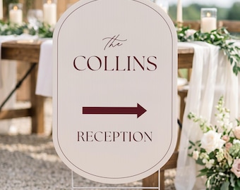 May include: An oval-shaped sign with a light beige background and a thin dark red border. The text reads "The COLLINS" in a mix of script and serif fonts, followed by a dark red arrow pointing right and the word "RECEPTION" in serif font.