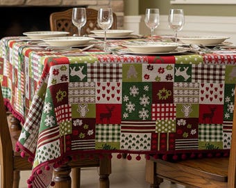 May include: A festive Christmas-themed tablecloth with a patchwork design. The tablecloth features squares with reindeer, snowflakes, and heart patterns in red, green, and white. The edges are trimmed with red pom-poms. The table is set with plates, glasses, and silverware.