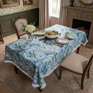 May include: A dining table set with a blue, green, and white marbled tablecloth. The table is set with plates, silverware, and a salad bowl. Two chairs are positioned around the table, and a vase of white flowers sits on the table.