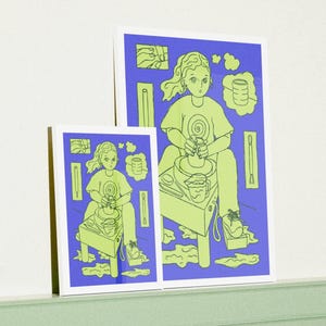Op de afbeelding: Twee ingelijste kunstdrukken met een limoengroene en blauwe illustratie van een persoon die op een pottenbakkerswiel werkt. De persoon draagt een limoengroen t-shirt en zit op een limoengroene kruk. De achtergrond is blauw.