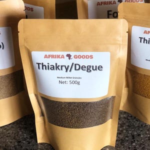 May include: A close-up of several brown paper pouches of "Thiakry/Degue" millet granules. Each pouch has a white label with the brand "AFRIKA GOODS" and the net weight of 500g. The granules are visible through the clear portion of the pouch.
