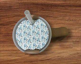 May include: A white and blue patterned lid with a straw hole for a tumbler. The lid has a repeating pattern of blue scrubs with a stethoscope and the word "Scrubs" on a white background.