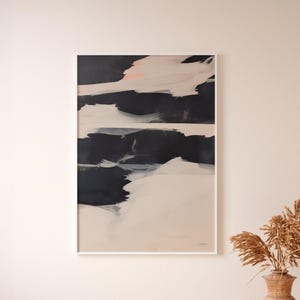 May include: Abstract art print in a white frame. The artwork features bold brushstrokes of black, white, and beige, with a touch of pink. The composition is a modern, minimalist design, suitable for home decor.