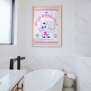 May include: A framed print with a cartoon toilet paper roll character that reads "Good Wipes Only." The print has a light wood frame and is displayed in a bathroom with a white bathtub and marble tile.