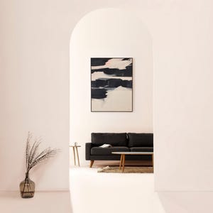 May include: An abstract artwork with black and white paint strokes is displayed above a dark grey sofa. A glass vase with dried plants and a small wooden side table are in the foreground. The room is painted in a soft pink hue.