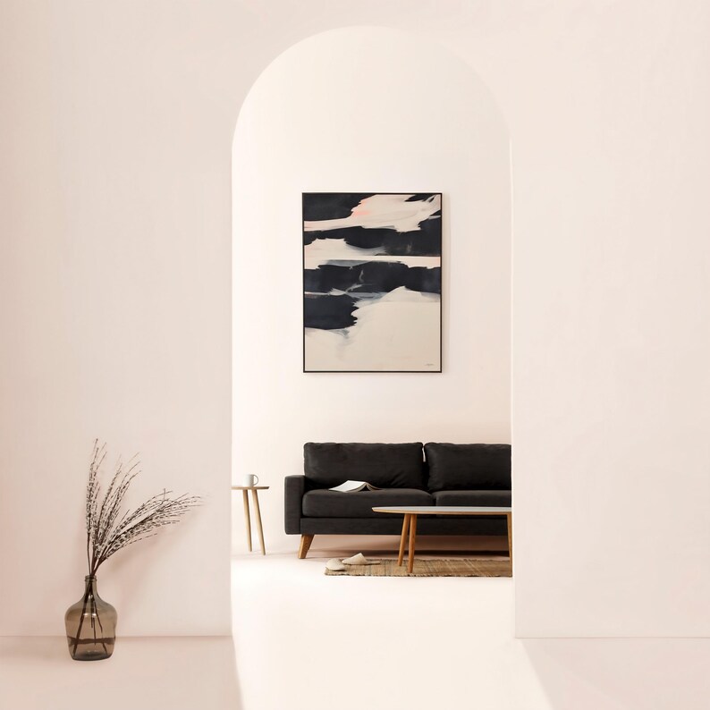 May include: An abstract artwork with black and white paint strokes is displayed above a dark grey sofa. A glass vase with dried plants and a small wooden side table are in the foreground. The room is painted in a soft pink hue.