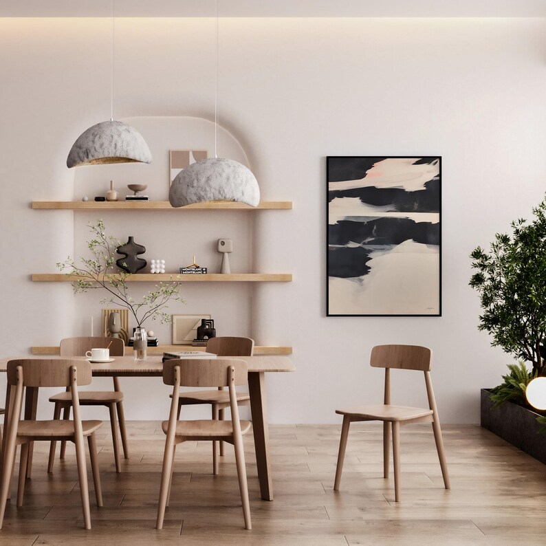 May include: A modern dining room with a wooden table and chairs, an abstract painting, and two pendant lights. The room has a neutral colour palette with natural wood tones. Decorative shelves display various objects, creating a minimalist aesthetic.
