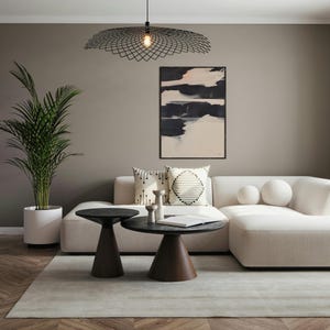 May include: A contemporary living room featuring a cream-coloured sofa, two dark brown side tables, and an abstract painting. A black geometric pendant light hangs overhead. A potted palm and decorative cushions complete the scene.