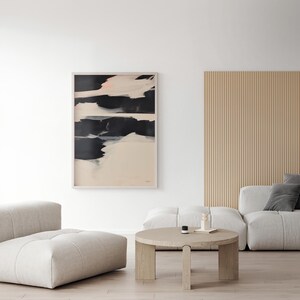 May include: Framed abstract art print with a light wood frame. The artwork displays striking black brushstrokes on a cream backdrop, with touches of pink. The print is displayed in a modern living room with neutral furniture.