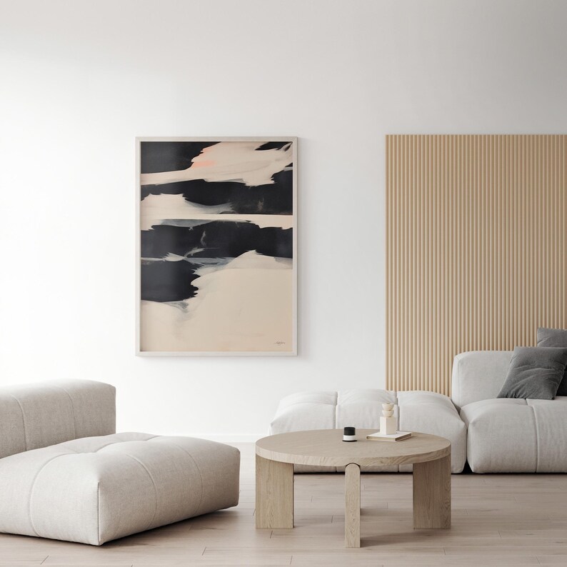 May include: Framed abstract art print with a light wood frame. The artwork displays striking black brushstrokes on a cream backdrop, with touches of pink. The print is displayed in a modern living room with neutral furniture.