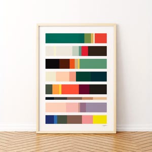 May include: A framed art print featuring a series of horizontal color blocks in various shades. The color palette includes greens, reds, browns, oranges, pinks, and blues. The artwork is displayed in a light wood frame.