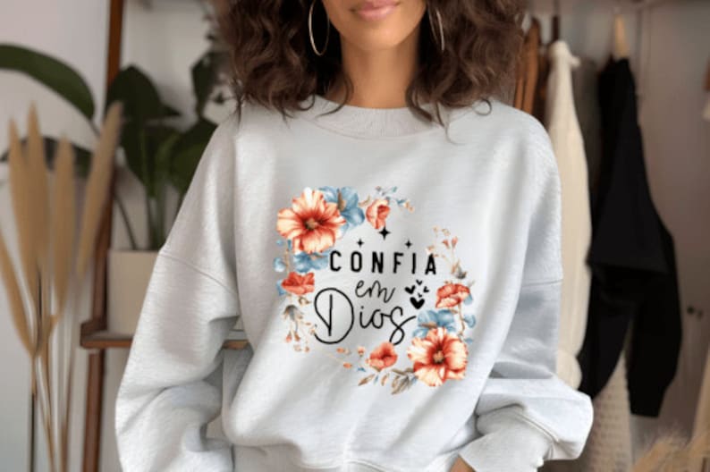 May include: A light gray sweatshirt with a floral design and the text "CONFIA en Dios" in black.