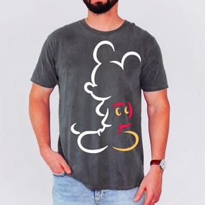May include: Dark gray t-shirt featuring a white outline of Mickey Mouse. The design includes red, yellow, and black accents. The shirt is a crew neck and has short sleeves.