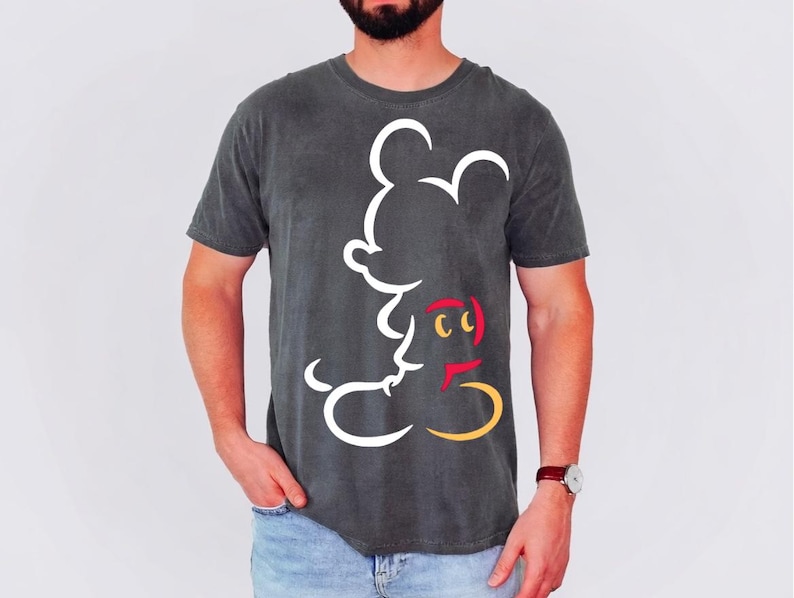 May include: Dark gray t-shirt featuring a white outline of Mickey Mouse. The design includes red, yellow, and black accents. The shirt is a crew neck and has short sleeves.