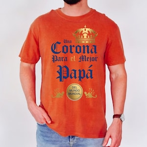 May include: Orange t-shirt with the text "Una Corona Para el Mejor Papá" in blue and a gold crown graphic. The shirt also features a gold emblem that says "Del Mundo Mundial".