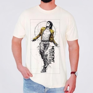 May include: A cream-colored short-sleeve t-shirt featuring a black and white sketch-style graphic of Michael Jackson in a yellow jacket. The design includes technical line drawings, a circular background element, and the text MICHAEL JACKSON.