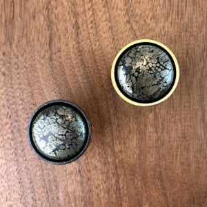 May include: Two round cabinet knobs with a black and gold finish. The knobs have a speckled, textured surface.